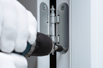 Repairman installing interior door and screwing door hinge with power screwdriver. - obrazy, fototapety, plakaty