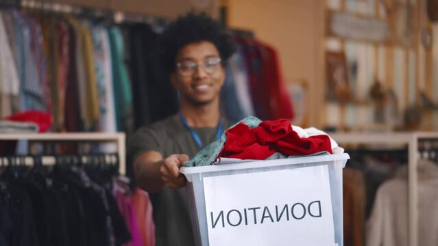 Happy African-American volunteer hold donation box with clothes and smile at camera. Realtime