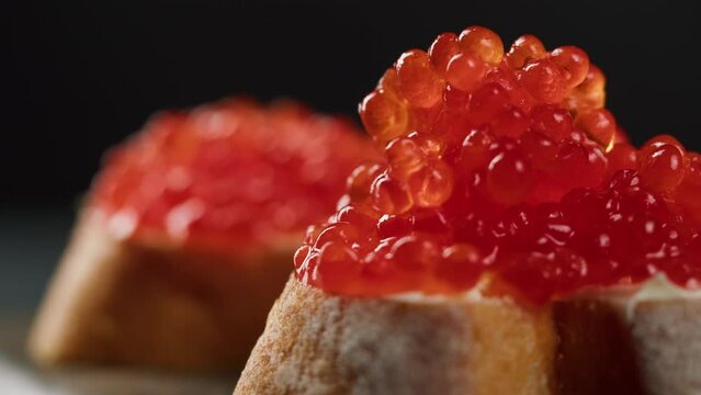Red caviar sandwiches close-up. Bread with salmon salted orange roe on black background. Raw seafood. Luxury delicacy food. Delicious and tasty fish products. Russian cuisine. Festive dinner,