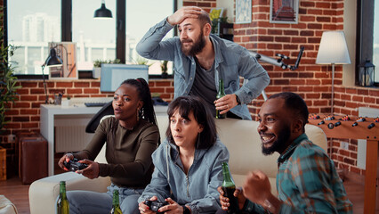 Group of friends playing video games on television console, having fun with gaming competition online at home gathering. Cheerful people meeting to play game on tv, drinking beer.