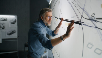 Senior automotive male designer creating sketch with duct tape on paper whiteboard, developing...