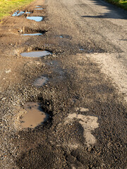 Pot holes filled with water on a small rural road. Dangerous road conditions