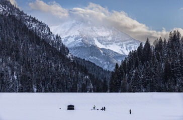 Winter mountain landscape with small figures of people ice fishing on reservoir below.