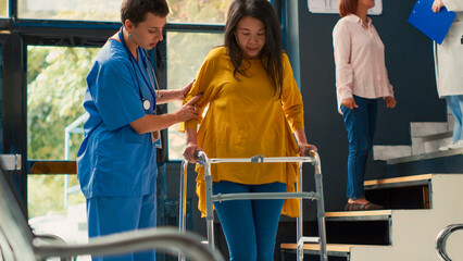 Nurse helping asian woman to walk with walking frame, suffering from physical injury and impairment. Injured patient with leg pain recovering after fracture and trauma. Handheld shot. © DC Studio