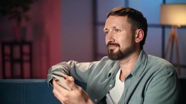 Smiling man smartphone chatting dating application browsing internet social networks evening home