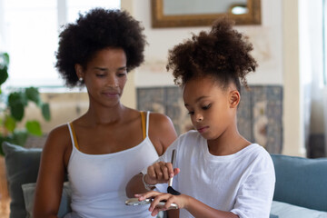 African American mother teaching daughter how apply makeup. Little girl with curly hair holding...