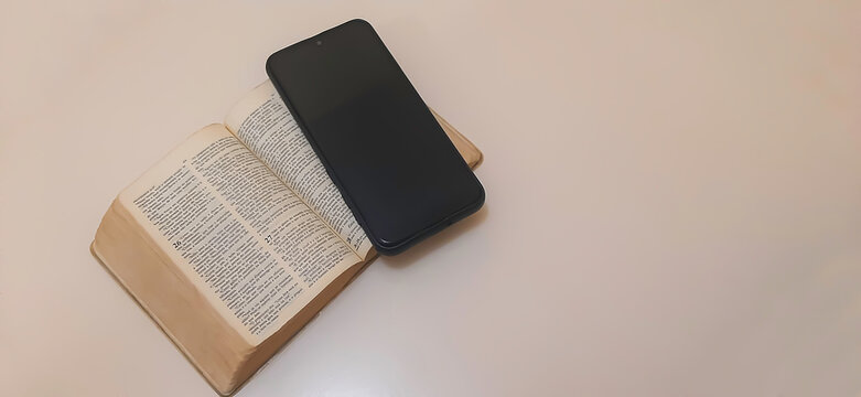 Mobile phone and holy bible on neutral background with copy space