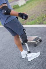 Sportsman with disability in street on sunny day. Man in casual clothes and sportive protection and skateboard. Sport, disability, training concept