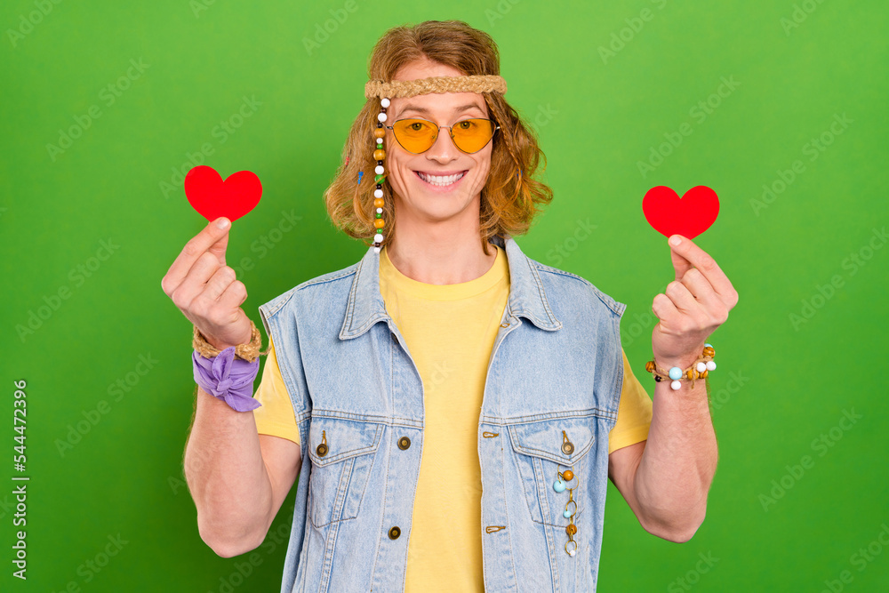 Sticker Portrait of positive handsome hippy person hold two little heart symbol isolated on green color background