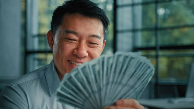 Wealthy asiana korean man successful rich businessman banker investor hold money banknotes dollar currency win in lottery cash salary bonus success profitable investment at stock exchange bank deposit