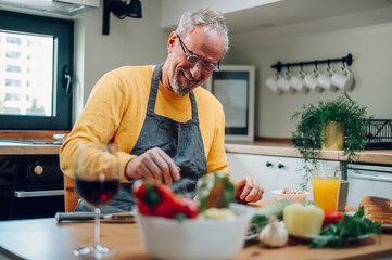 Senior man in apron preparing food at the kitchen counter and cooking a meal