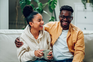 Multiracial couple relaxing on a couch at home and drinking coffee