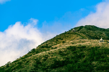 Huge Hill Hiking Path Up To Clouds / View to high grass meadow mountain with trail and small shelter huts up at cloudy sky (copy space) - 544475753