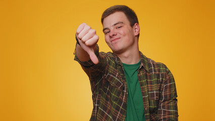 Dislike. Upset unhappy handsome man in shirt showing thumbs down sign gesture, expressing discontent, disapproval, dissatisfied, dislike. Young adult guy boy. Indoor studio shot on yellow background