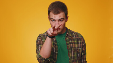 I am watching you. Man in casual green shirt pointing at his eyes and camera, show I am watching you gesture, spying on someone. Young adult guy boy isolated alone on yellow studio wall background