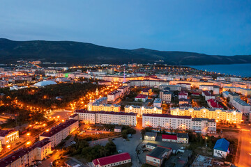 Night aerial photograph of a seaside port town. Top view of illuminated streets and buildings. Mountains and sea in the distance. City of Magadan, Magadan region, Far East of Russia.