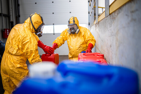 Industry workers in protective suits handling acids and aggressive substances in chemicals production factory.