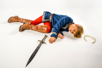 Young boy dressed up like a cosplay prince lying on the ground defeated in battle