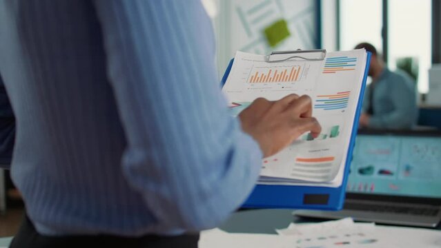 Closeup of african american woman hands holding clipboard with financial data and sales charts in startup office. Focused employee analyzing performance indicators reading business statistics.