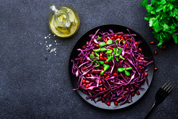 Vegan salad with red cabbage, parsley, pomegranate seeds, sunflower sprouts and olive oil dressing on black kitchen table background, top view
