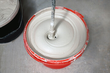 Mixing putty with electric mixer in red bucket indoors, above view