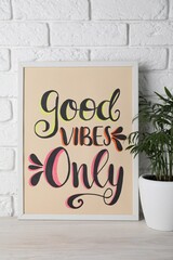 Board with phrase Good Vibes Only and houseplant on wooden table near white brick wall