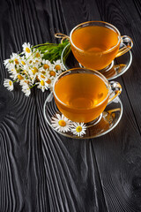 aromatic hot chamomile tea on a black rustic wooden background