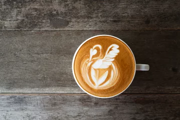 Schilderijen op glas Latte art coffee with swan shape in coffee cup on wooden background, Hot drink, Table top view © nungning20