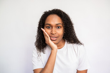 Fototapeta na wymiar Portrait of surprised young woman looking at camera over white background. Curious African American lady wearing white T-shirt listening with interest. Curiosity concept