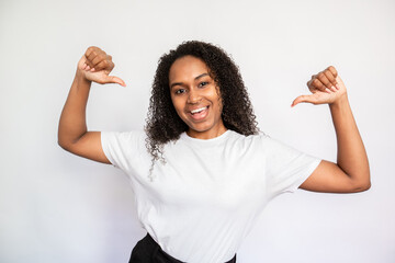Portrait of self assured young woman pointing thumbs at herself over white background. African...