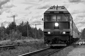 Diesel locomotive rides on rails with passenger cars, black and white photo. Russian passenger train.