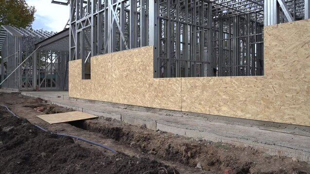 A dynamic handheld panning shot of an unfinished house or uncompleted structure with visible steel frames and plywood sheathing.