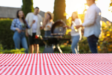 Empty table and blurred view of friends having barbecue party outdoors. Space for text