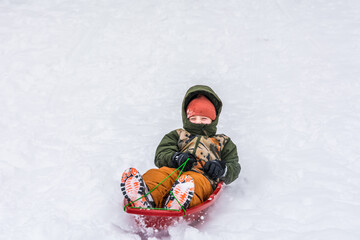 Fototapeta na wymiar The boy slides from the snowy hill on a speedy sled