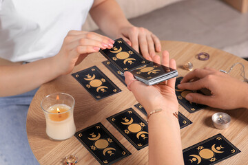 Woman pulling one tarot card at table indoors, closeup. Fortune telling
