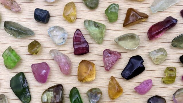 Tourmaline rare jewel stones texture on light varnished wood background. Moving right seamless loop backdrop.