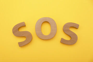Abbreviation SOS made of wooden letters on yellow background, top view