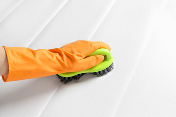 Woman in orange gloves cleaning white mattress with brush, closeup