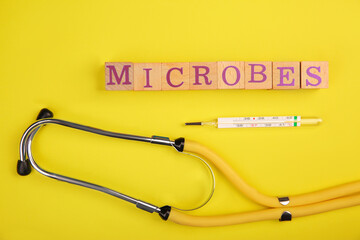 Word Microbes made with wooden cubes, syringe and stethoscope on yellow background, top view