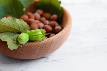 Bowl with hazelnuts and leaves on white wooden table, closeup. Space for text
