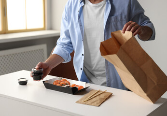 Man unpacking his order from sushi restaurant at table in room, closeup