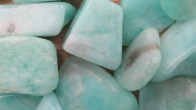 Amazonite jewel heap on light wood texture. Pile mineral pebbles background. Moving right seamless loop backdrop.