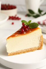 Piece of delicious caramel cheesecake with red currants and mint served on white marble table