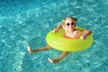 Happy little girl with inflatable ring in outdoor swimming pool on sunny day © New Africa