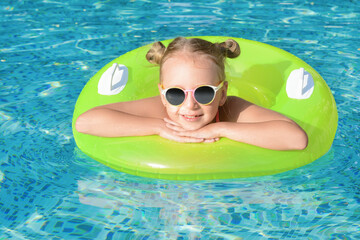 Happy little girl with inflatable ring in outdoor swimming pool on sunny day - Powered by Adobe