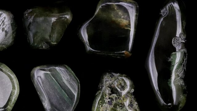 Green rutilated rare jewel stones texture on black background. Moving right seamless loop backdrop.