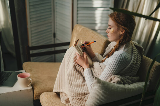 Cute lady with eyes patches at home writing notes on a diary while relaxing taking a break, enjoying home lifestyle. Resting, vacation, beauty treatment