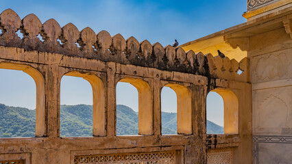 The ancient Amber Fort in India. Orange fortress wall with carved decorations. Green mountains and...