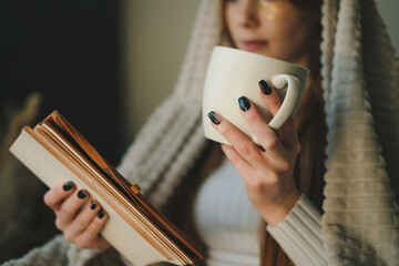 Woman sitting alone on sofa drinking a cup of coffee working or studying read book, relaxing, during free time indoors. Beautiful for lifestyle design. Happy
