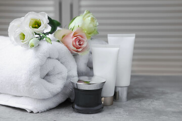 Towels, cosmetic products and flowers on grey table indoors